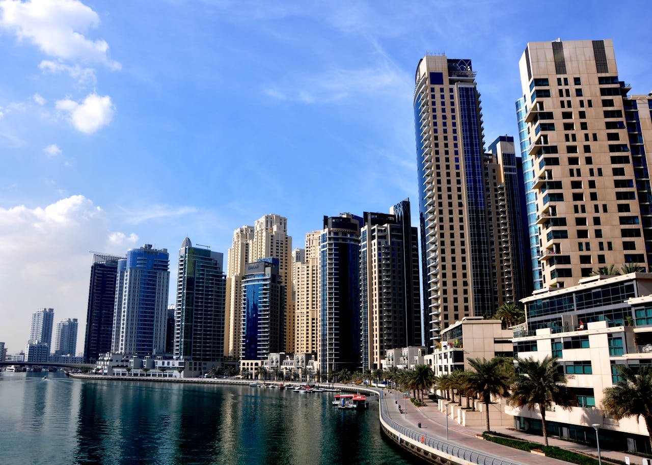 View of towering skyscrapers reflecting in calm marina waters under a blue sky.