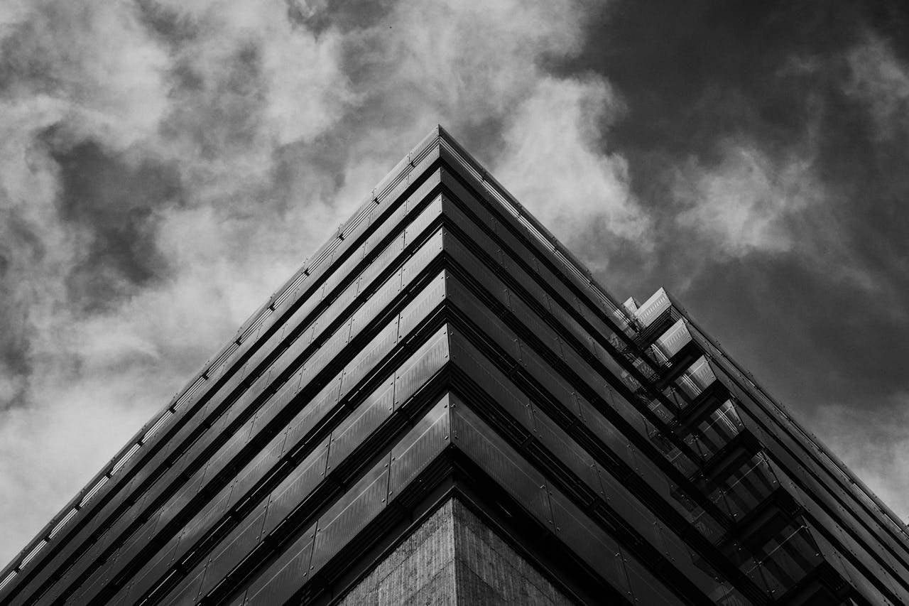 Black and white photo of a modern glass building against dramatic sky in Budapest.